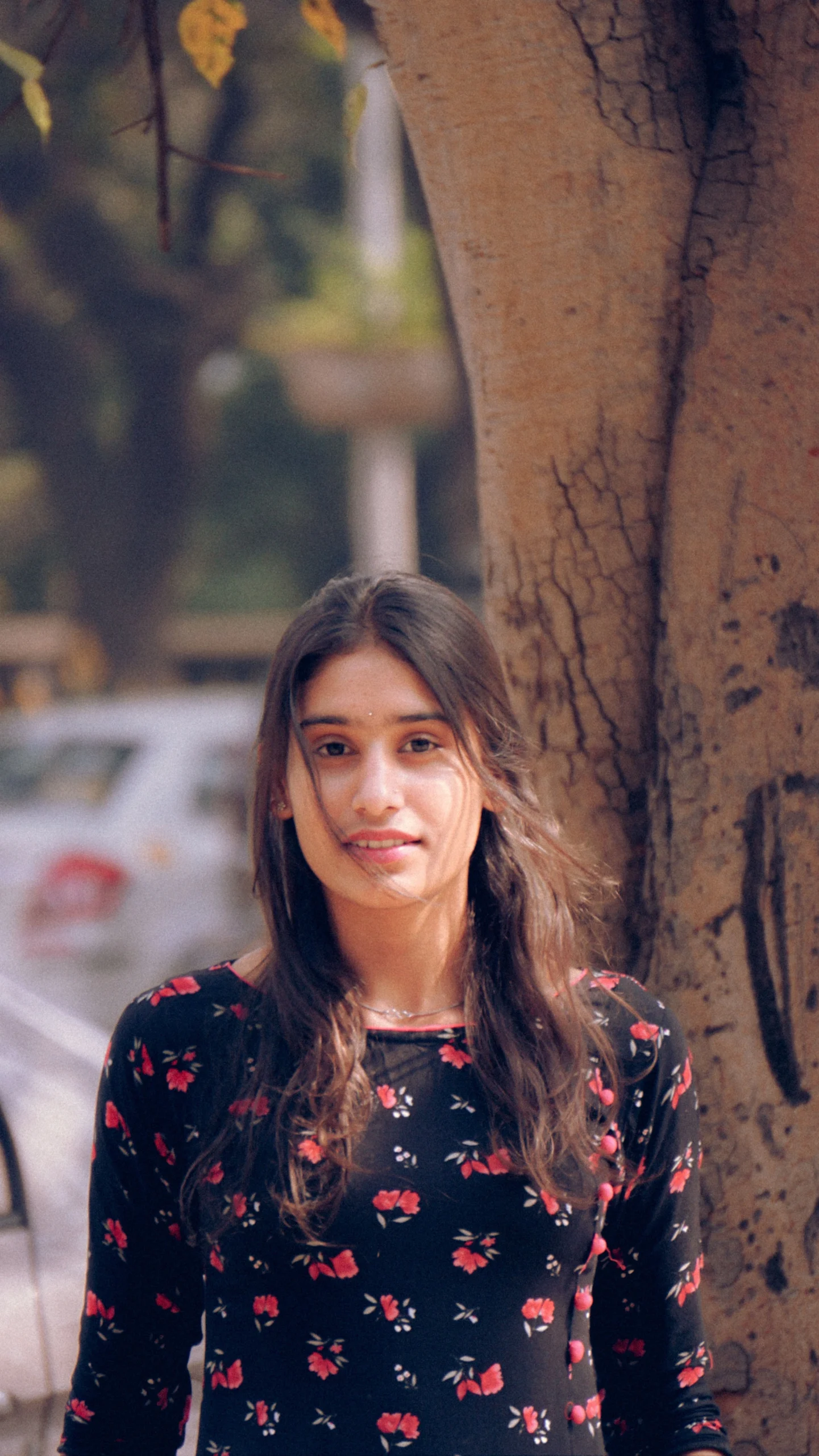Young woman standing outdoors beside a tree wearing a floral dress